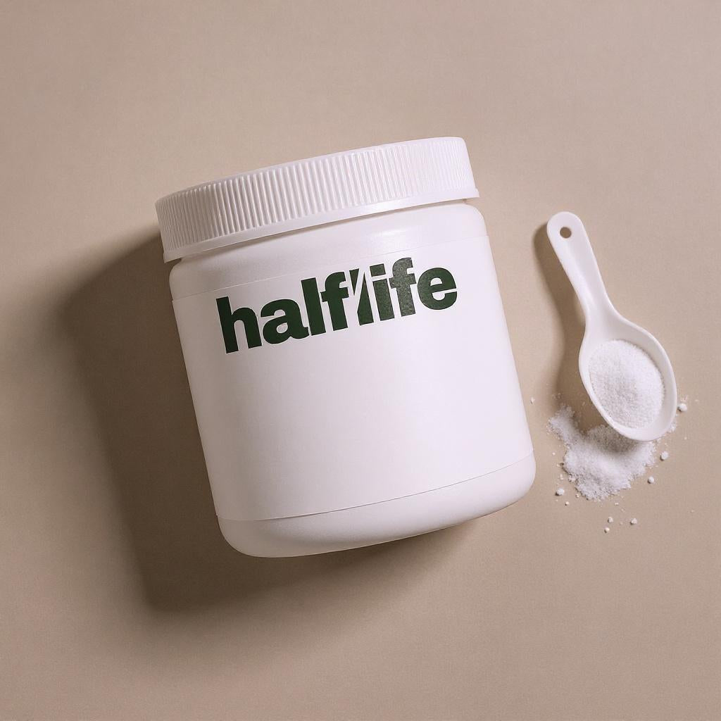 HALF/LIFE creatine tub on a paper-white backdrop with a small pile of creatine powder, documentary studio photograph
